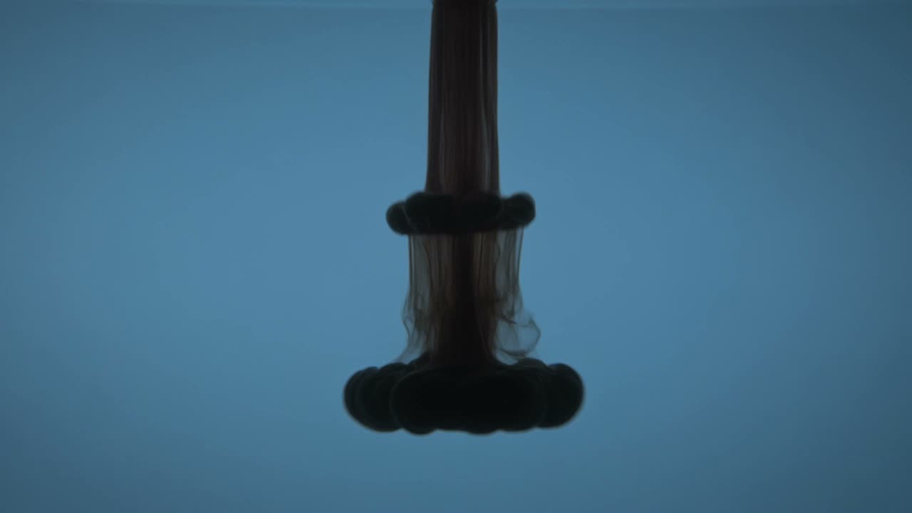 Still frame: black ink blooming downward through klein-blue water