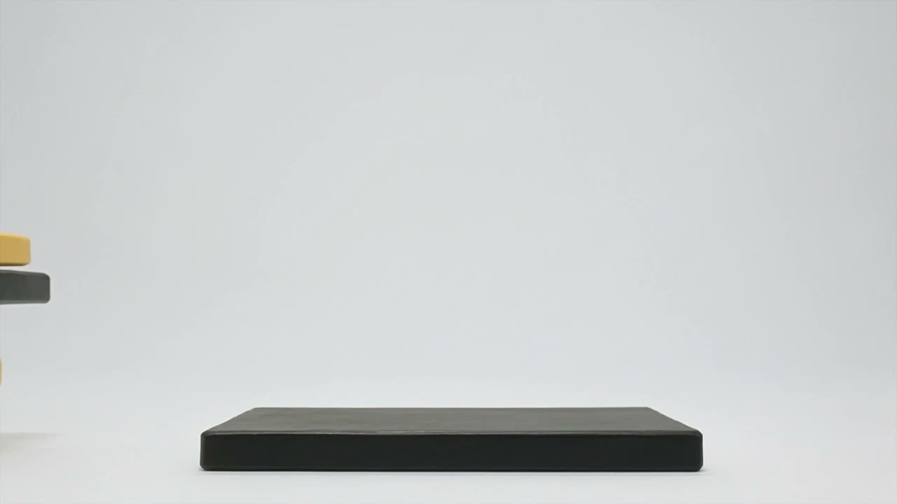 Still frame: painted yellow and black wooden slabs stacked on a pale seamless